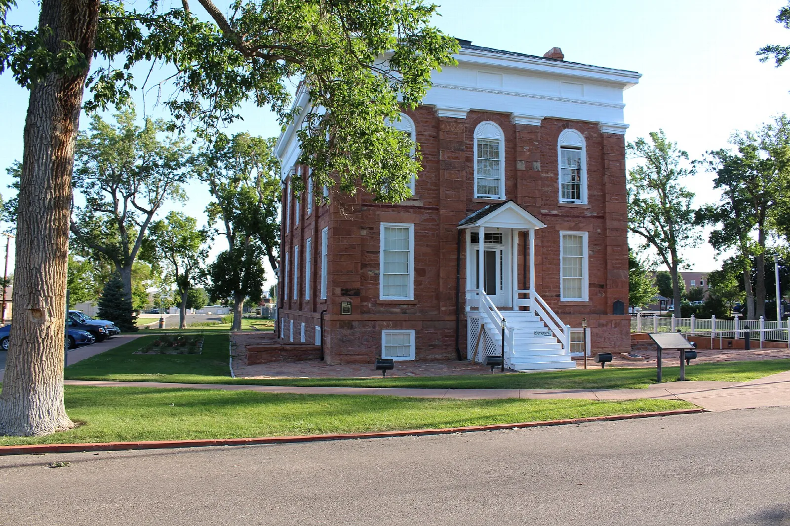 Red brick statehouse seen at an angle behind a tree and a lawn
