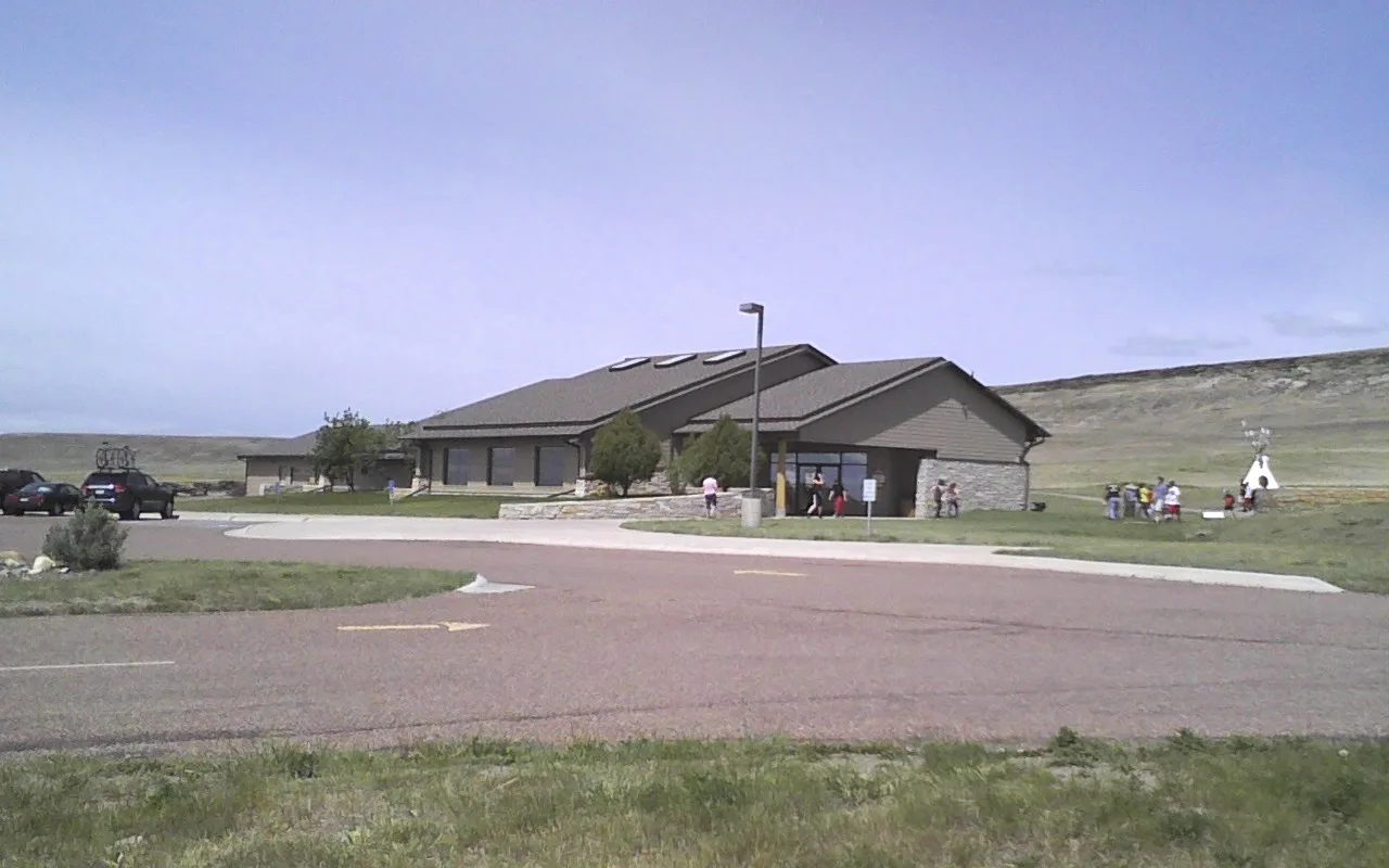 Low visitor center building beside a parking area, hill behind