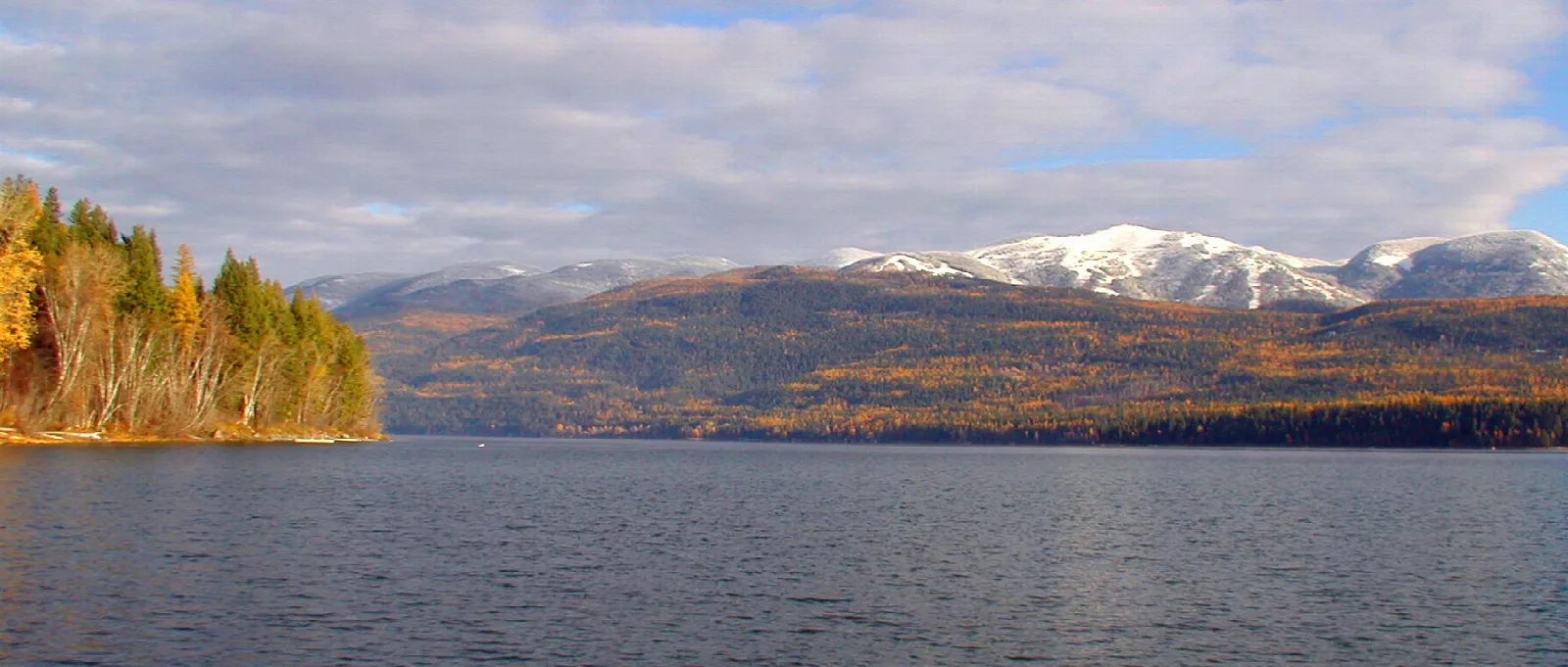 Lake in autumn with golden trees and snowy mountains behind
