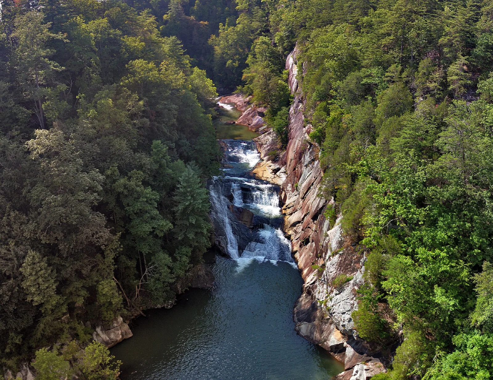 Waterfall dropping into a green pool between steep rock walls