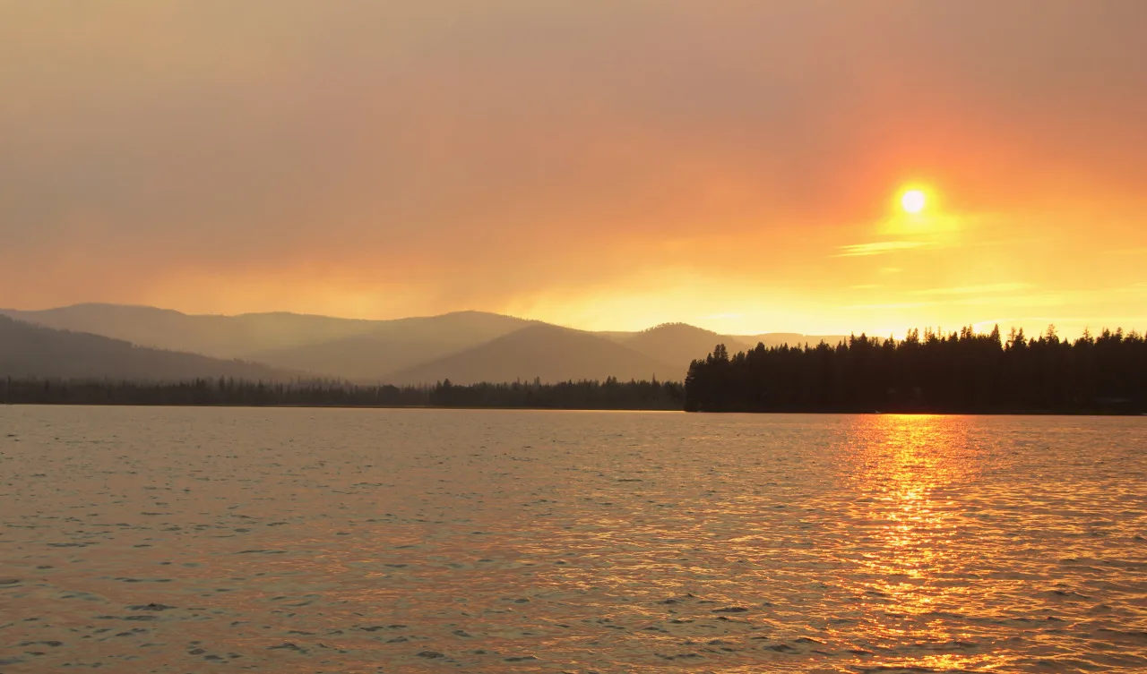 Orange smoky sunset over a lake and tree-lined hills