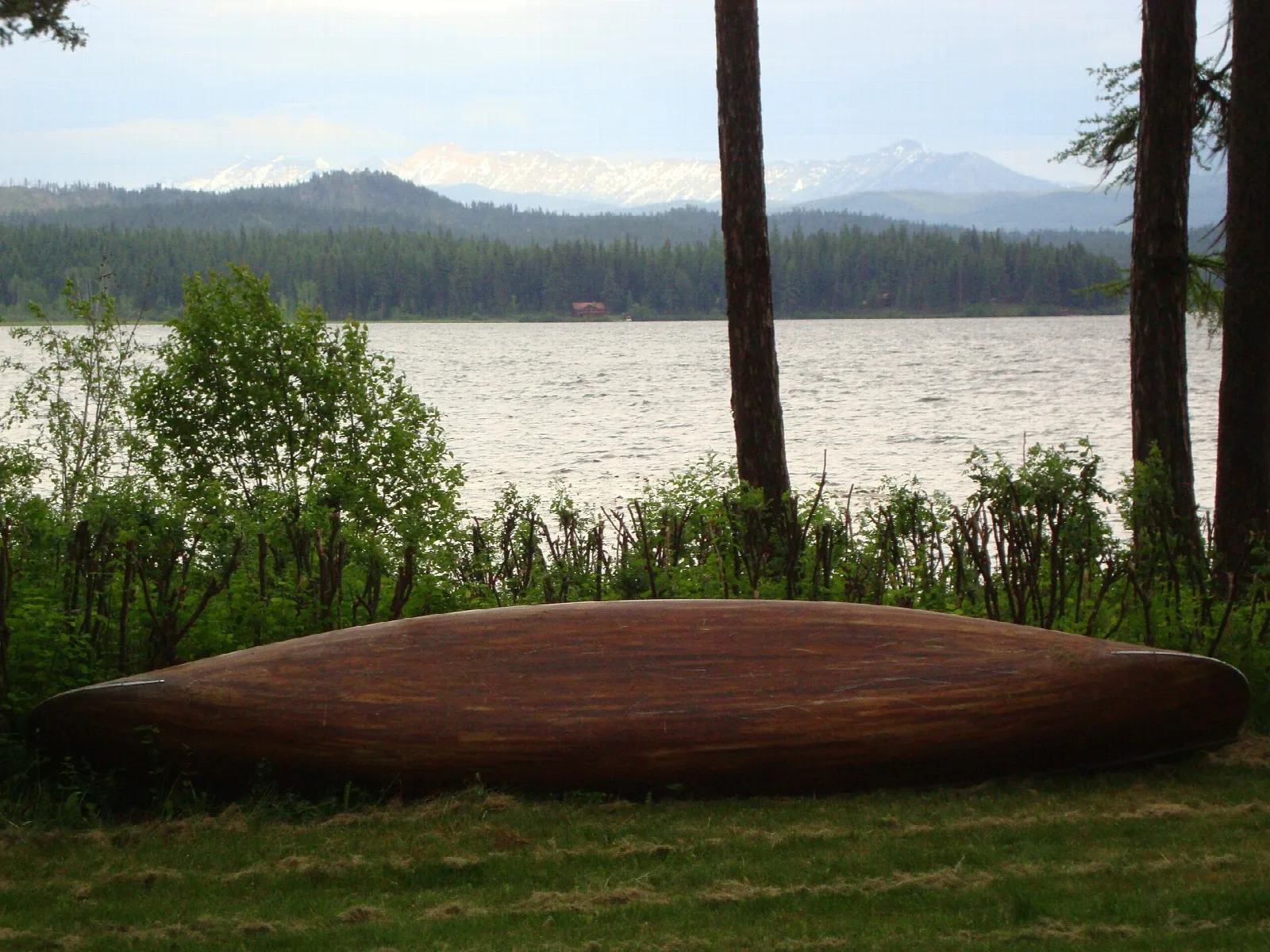 Wooden canoe on the grass by a lake with mountains beyond