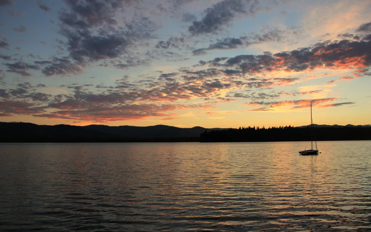 Sunset sky over a calm lake with a sailboat on the horizon