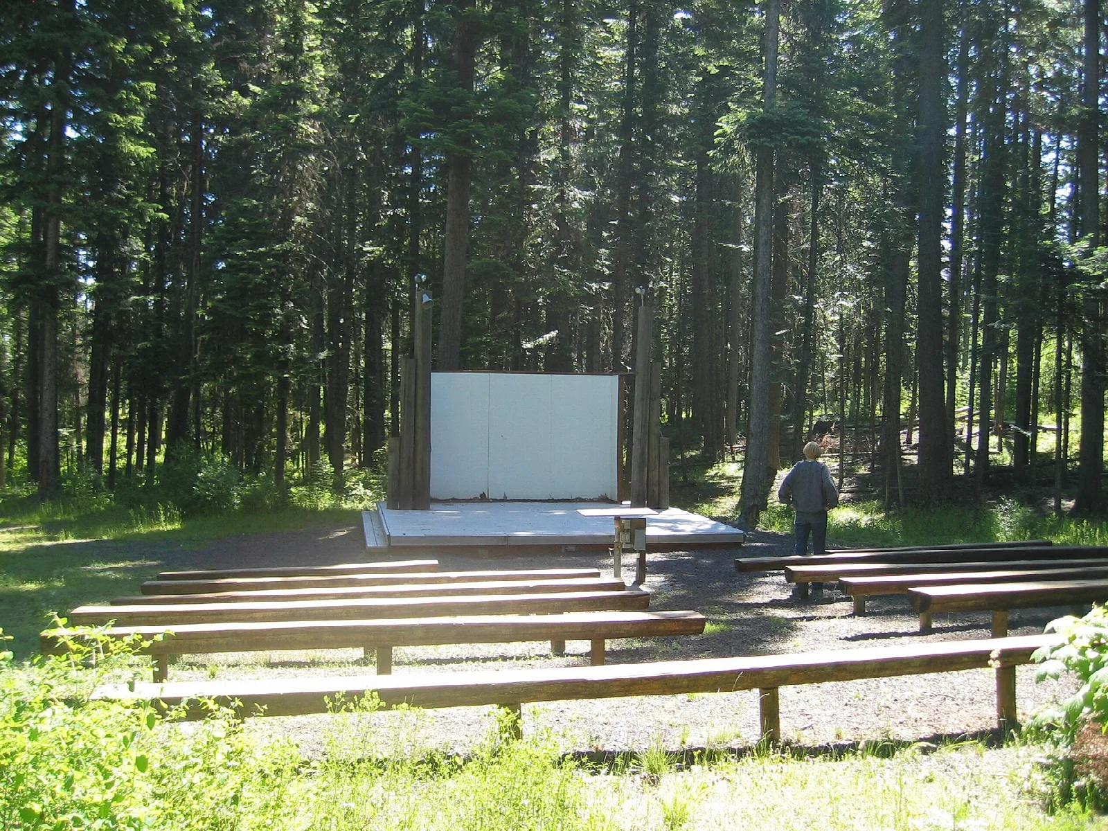 Outdoor amphitheater with wooden benches facing a screen in the forest