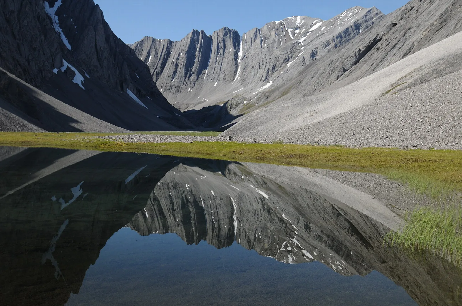 Steep gray mountains mirrored in a still tarn in a hidden valley