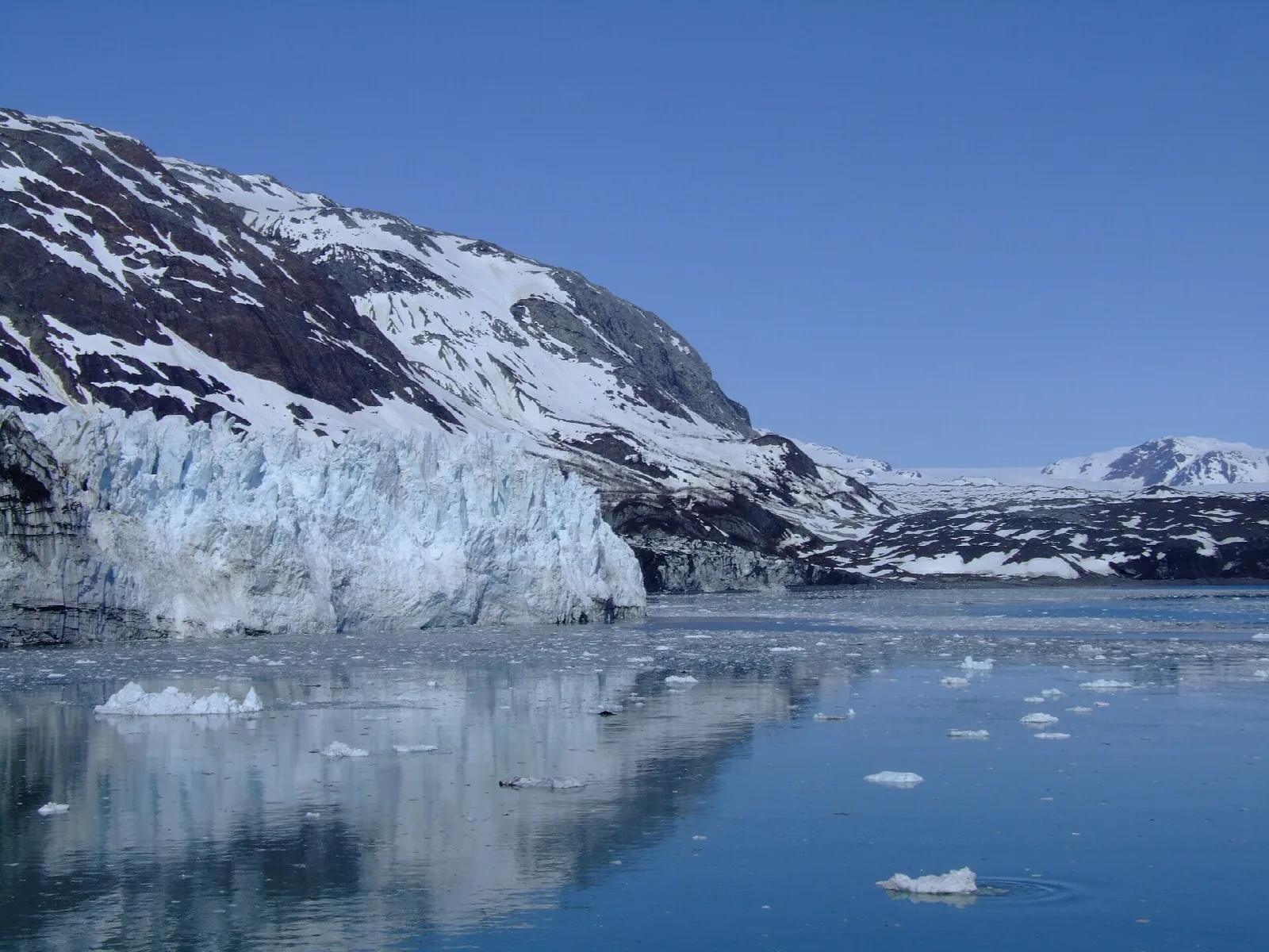 The tall, fractured ice face of a tidewater glacier meeting calm water below snowy peaks