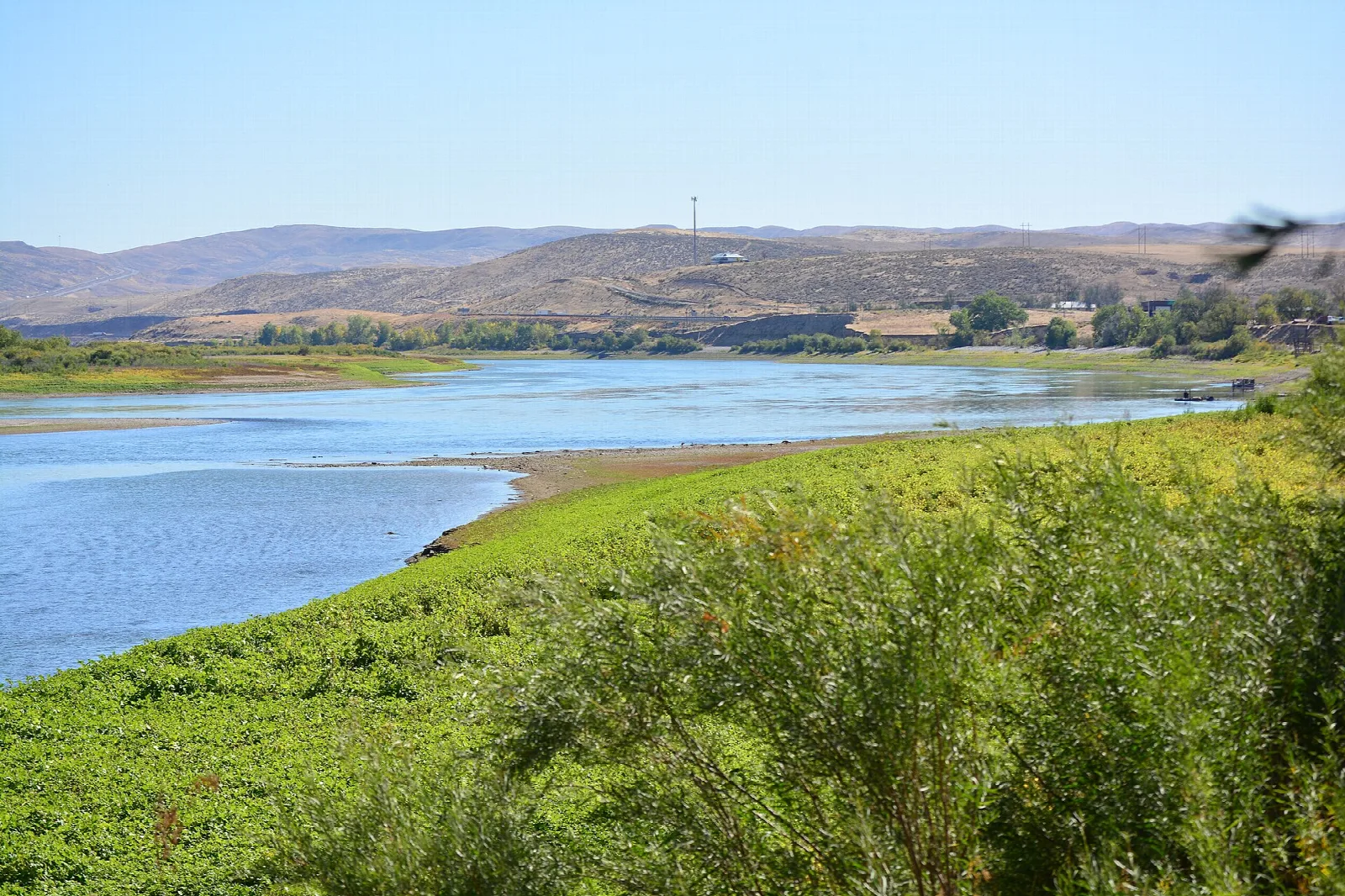 Wide blue river and green shore below brown desert hills