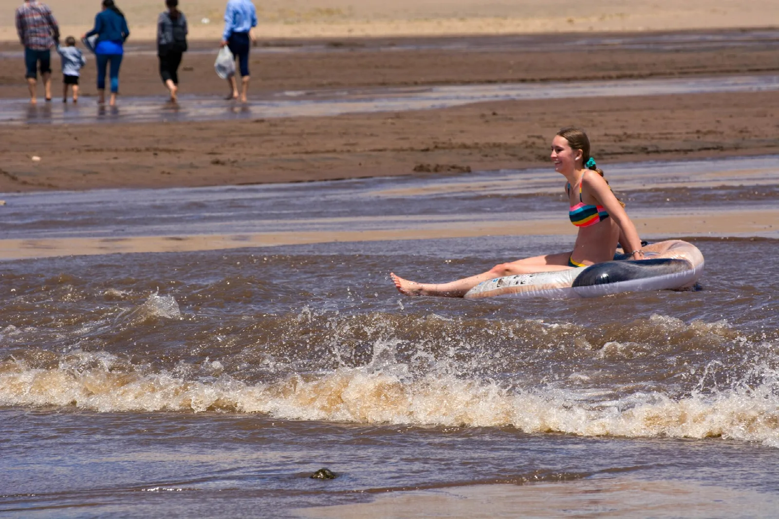A visitor riding a float on the shallow waves of a creek beside the dunes