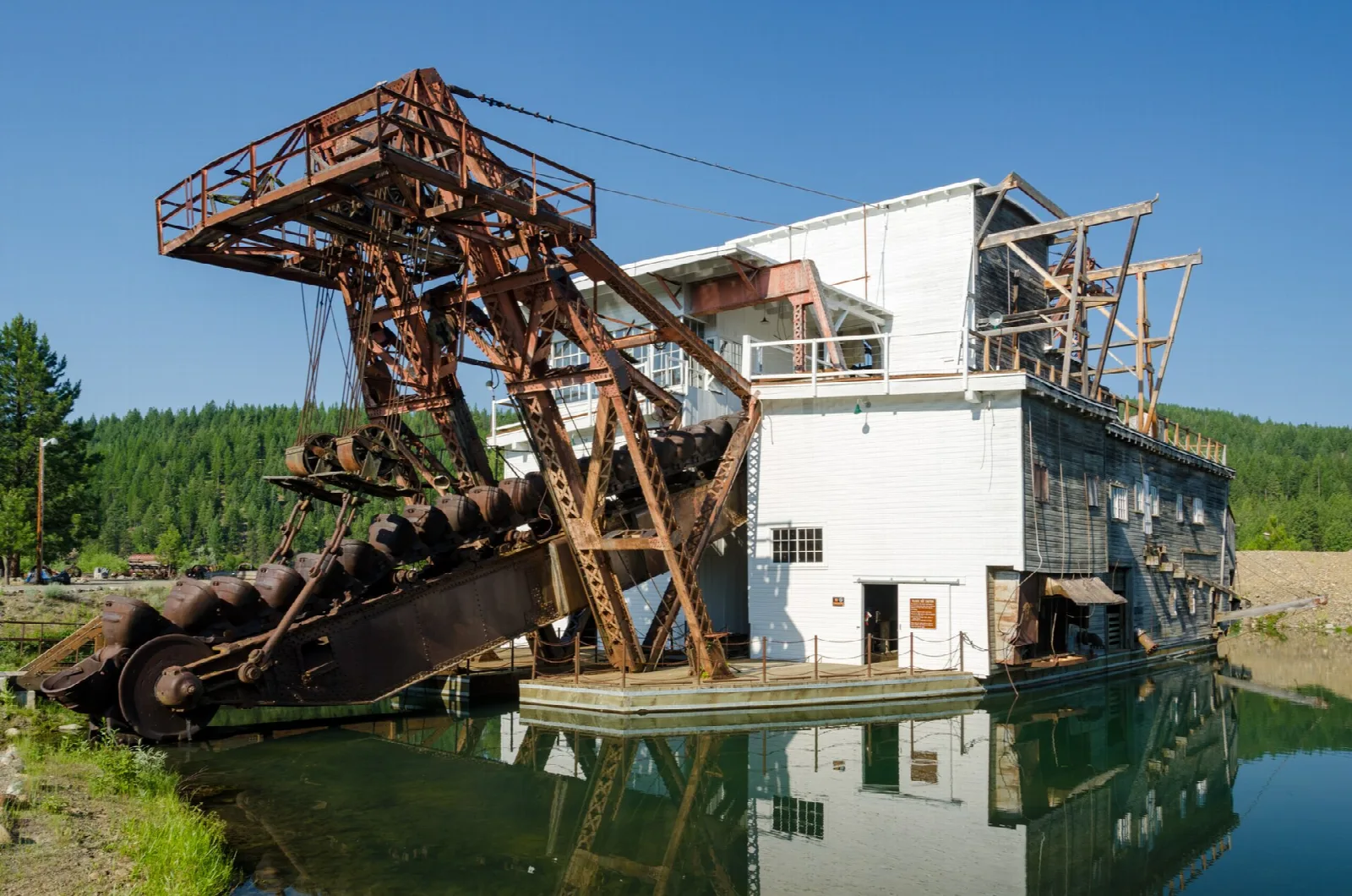 Rusty gold dredge with a long digging ladder sitting in a green pond