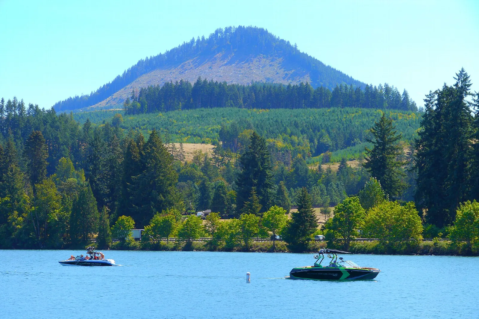 Boats on a blue lake below a forested mountain