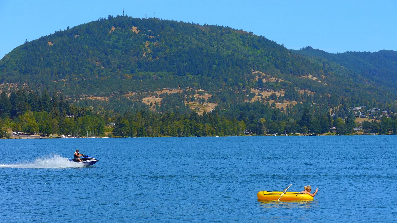 Jet ski and a yellow raft on blue water below a hill