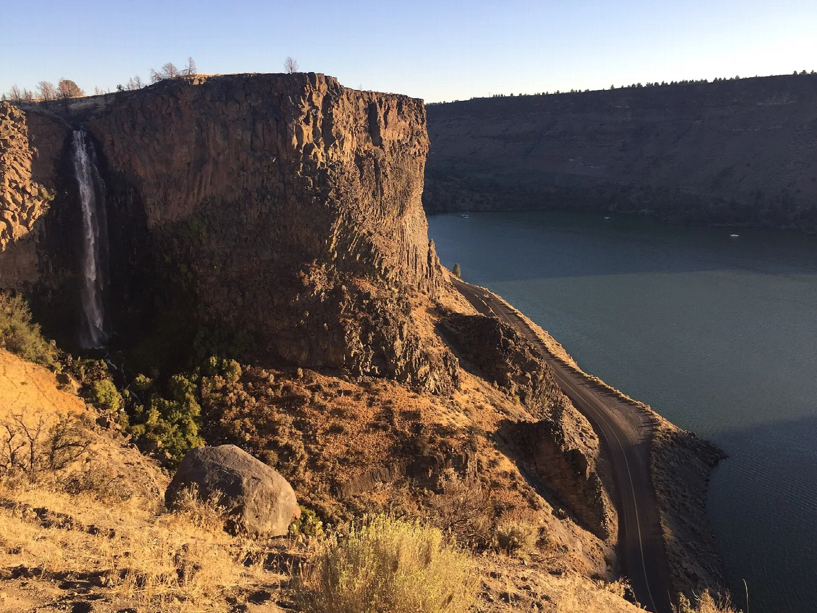 Dark basalt cliff with a thin waterfall dropping to a lake