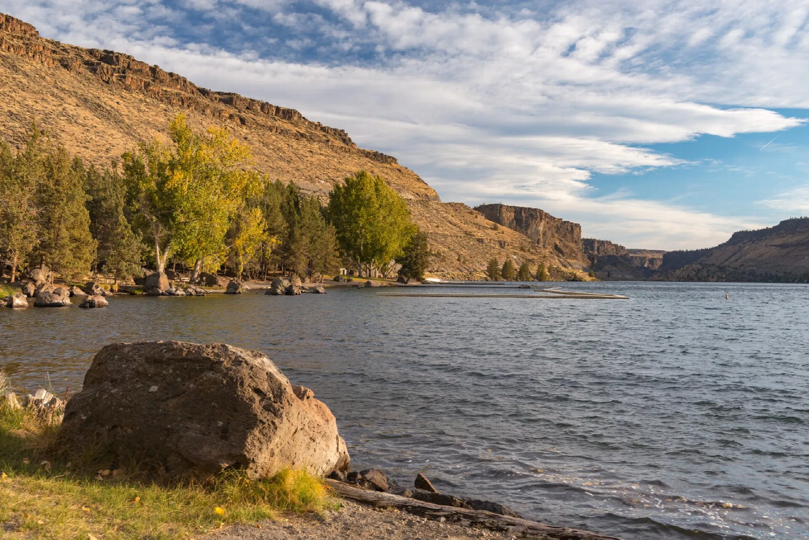 Lake shore with a large boulder and golden trees under canyon walls