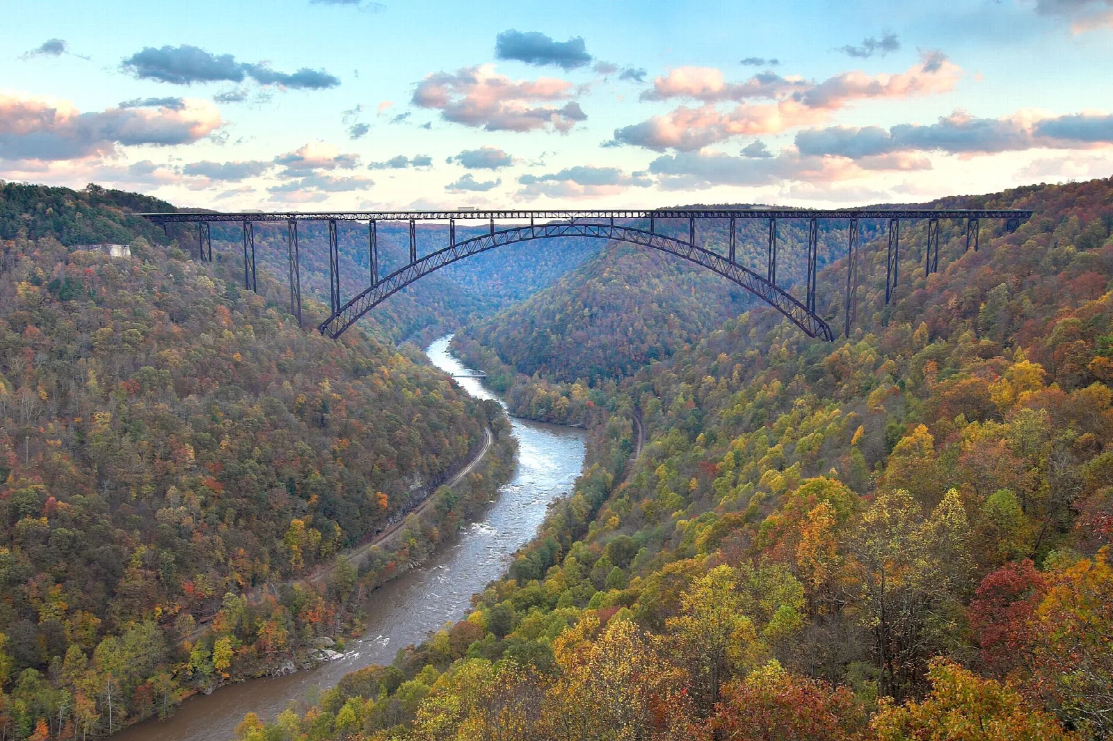 A steel arch bridge spanning a deep gorge of autumn forest, the river far below