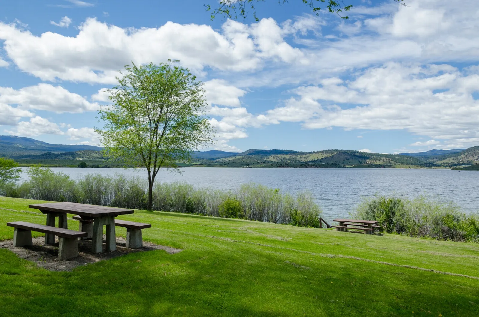 Picnic table on a lawn beside a wide lake with hills beyond