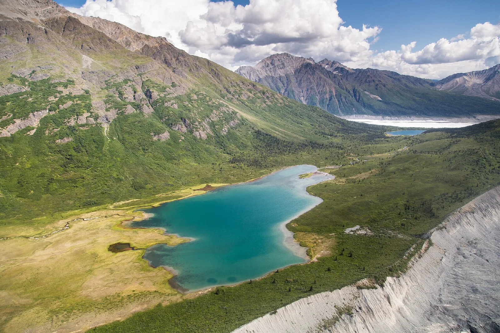 A turquoise lake in a green alpine basin beneath glaciers