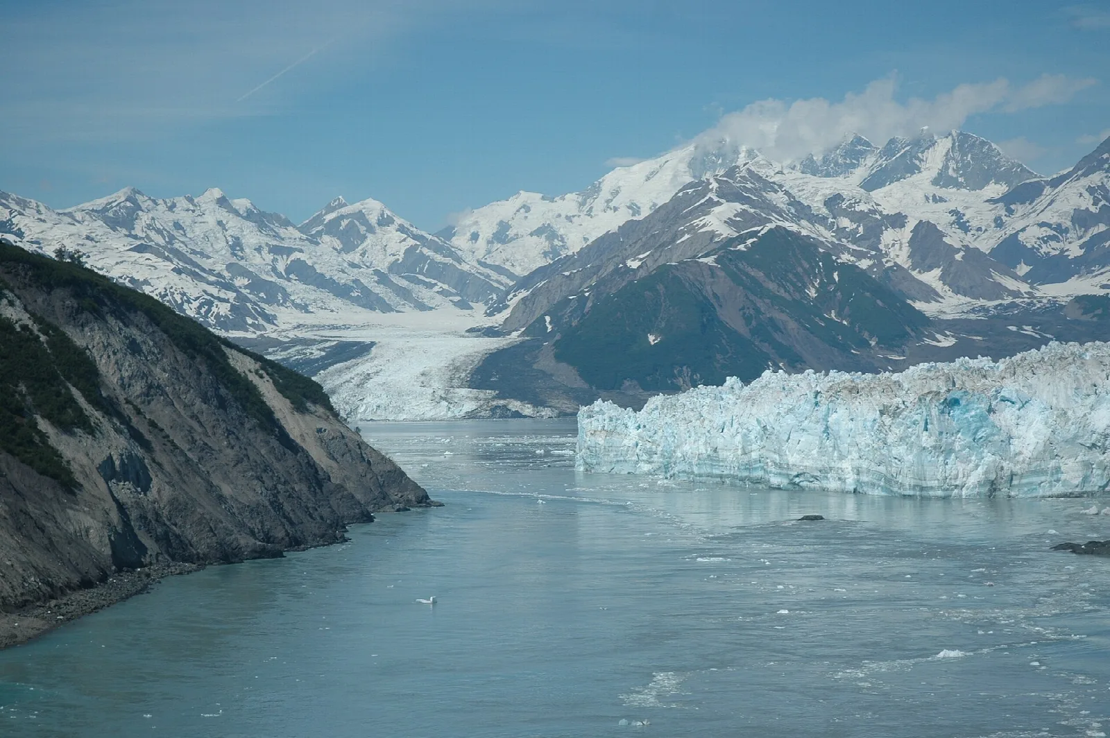 A massive tidewater glacier meeting a fjord below snow-covered mountains