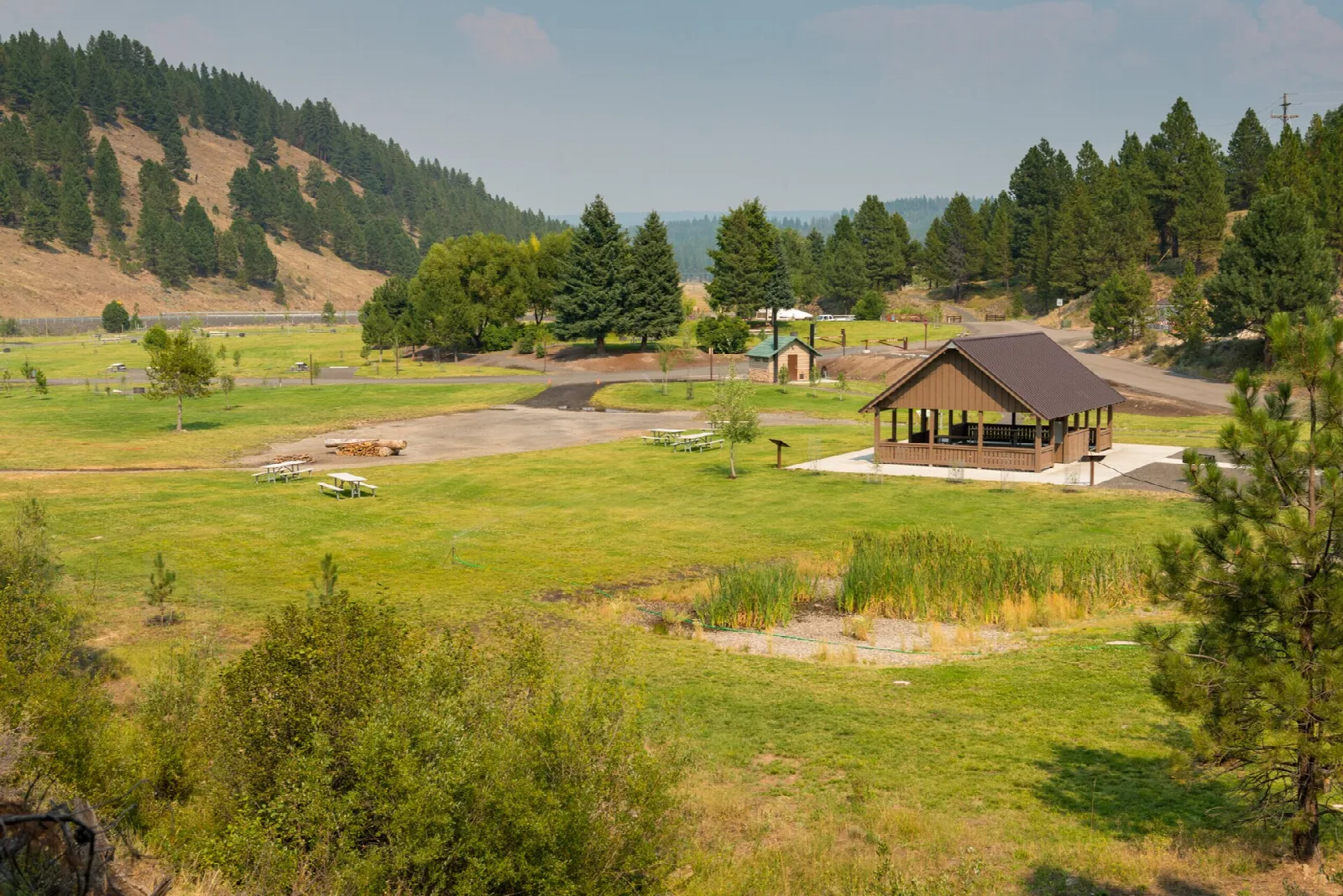Picnic shelter on a green lawn with forested hills behind
