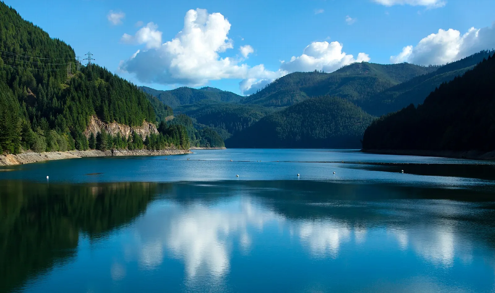 Blue lake with cloud reflections, forested ridges and mountains beyond
