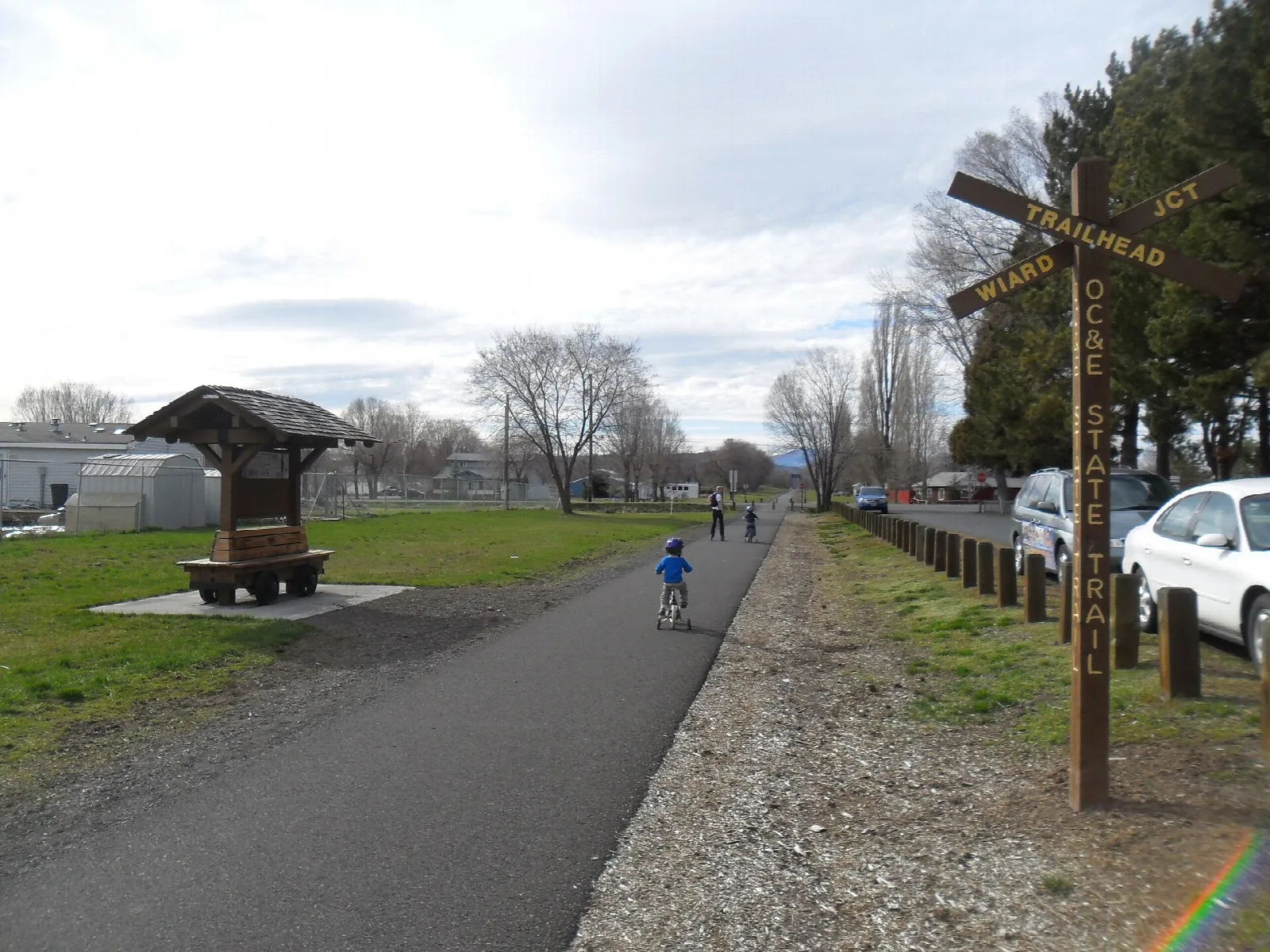 Paved trail beside a railroad-themed post and gravel shoulder in town