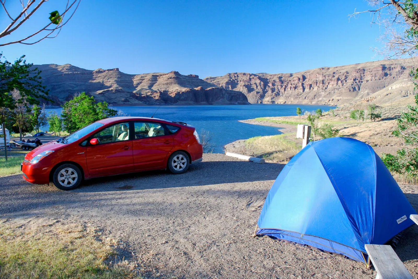 Blue tent and car at a campsite above a lake with canyon cliffs