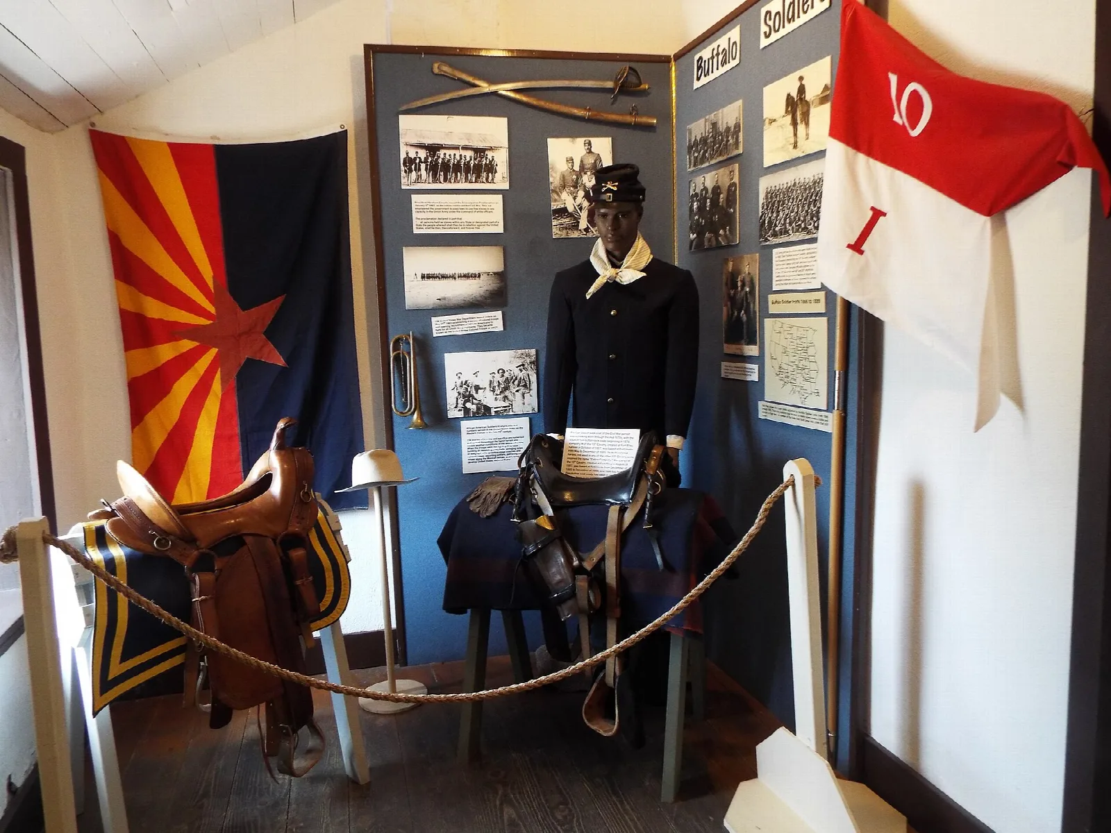 Museum display with a mannequin in a blue uniform, saddle and Arizona flag