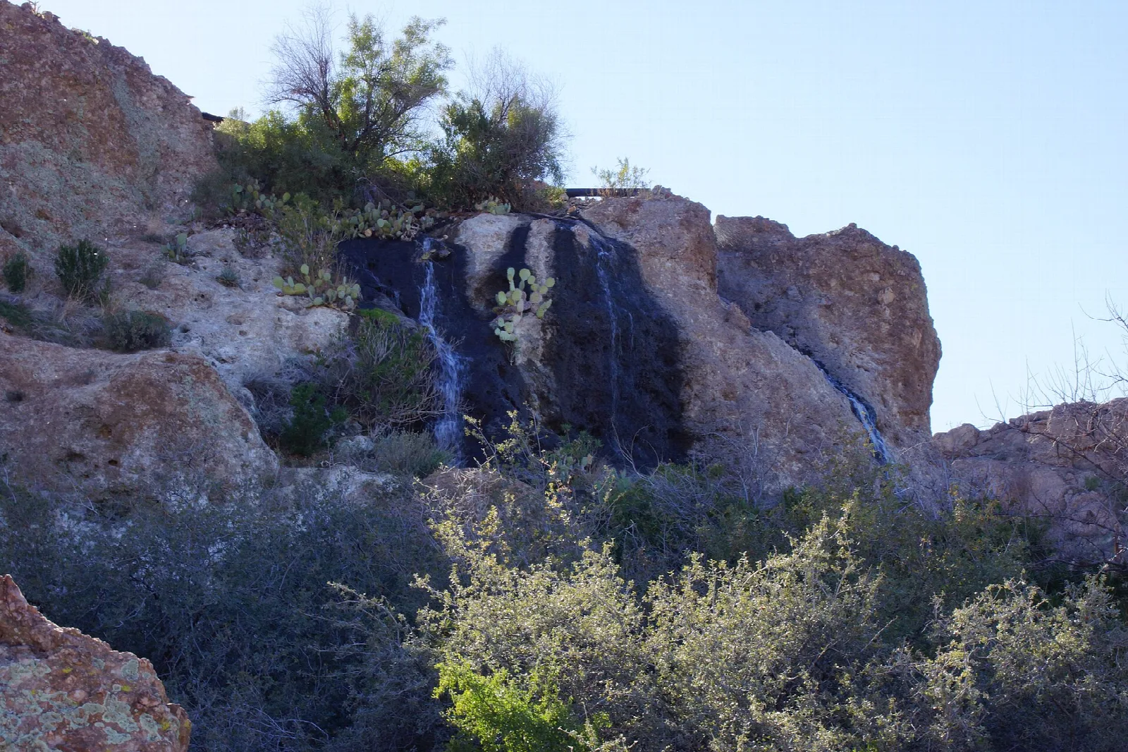 Small waterfall trickling over dark rock into desert scrub
