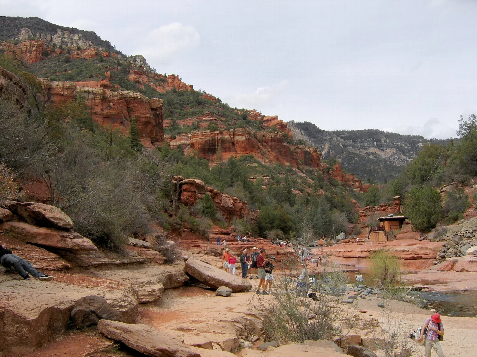 Visitors on red rock ledges beside Oak Creek in a canyon
