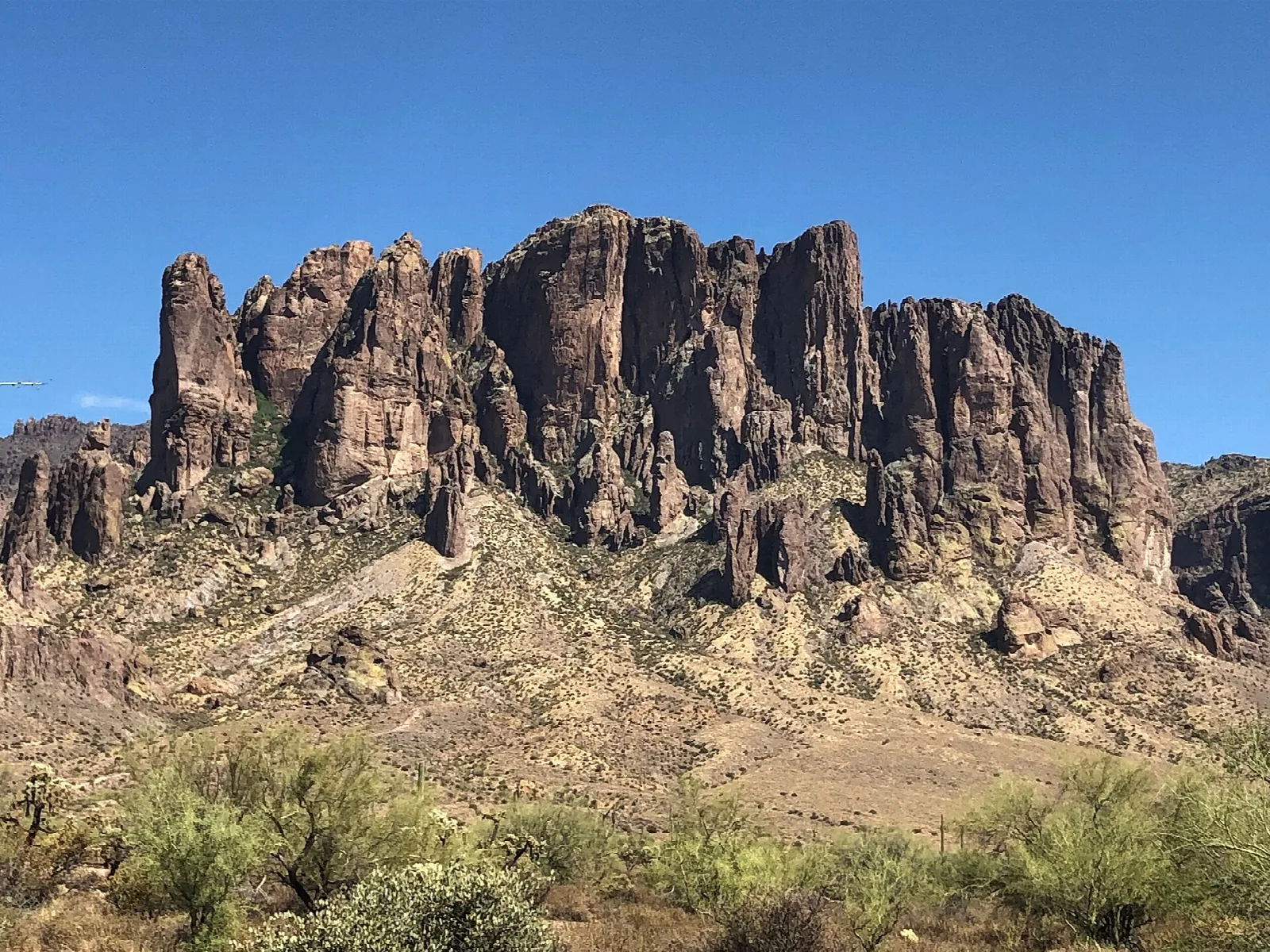 Jagged Superstition Mountain cliffs above desert scrub under blue sky
