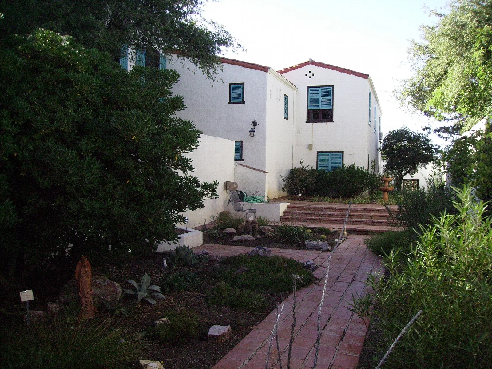 White Mediterranean-style ranch house behind a garden and brick path