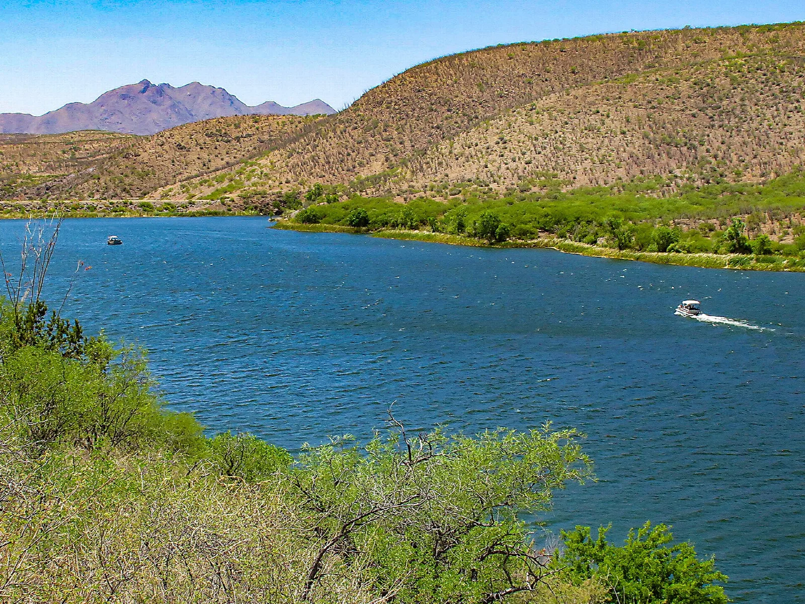 Blue lake with boats below green and tan hills