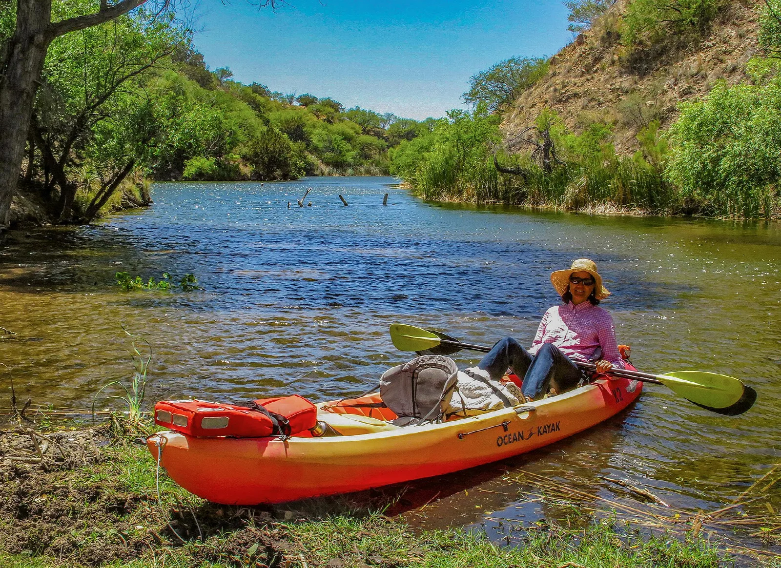 Person in an orange kayak on a green-banked lake