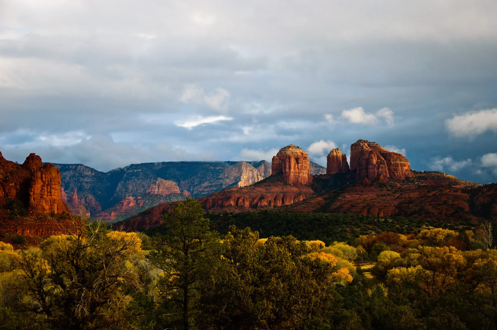 Red rock buttes under dramatic clouds with golden brush in front