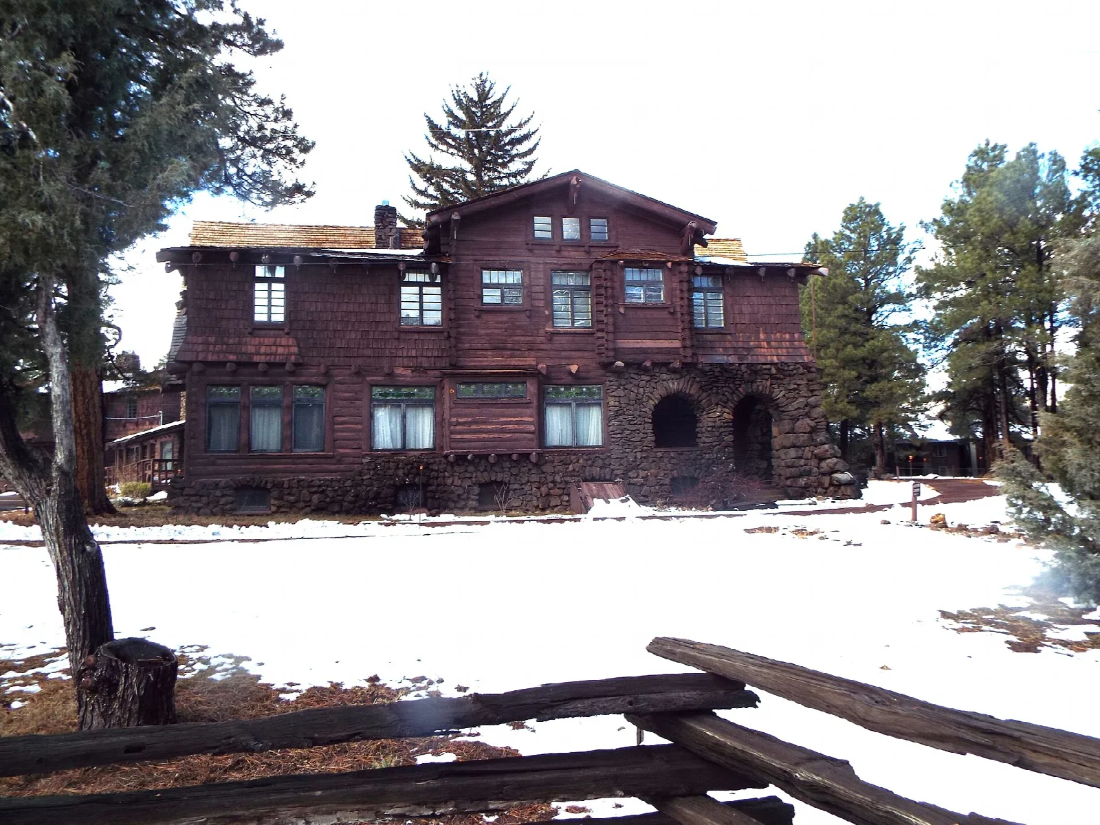 Dark-red timber mansion seen across a snowy yard behind a split-rail fence
