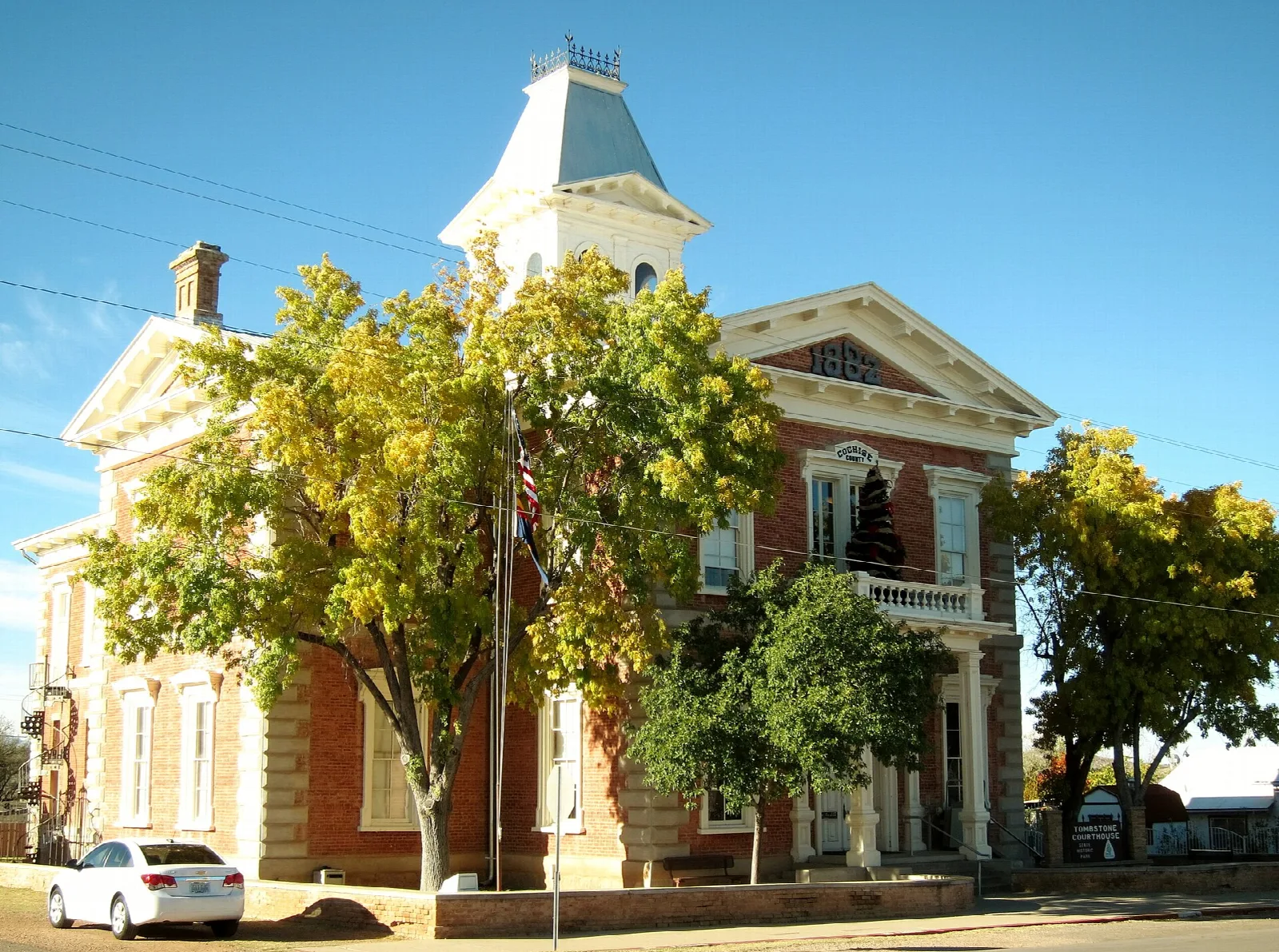 Brick courthouse with a cupola seen from the street corner, with fall-colored trees