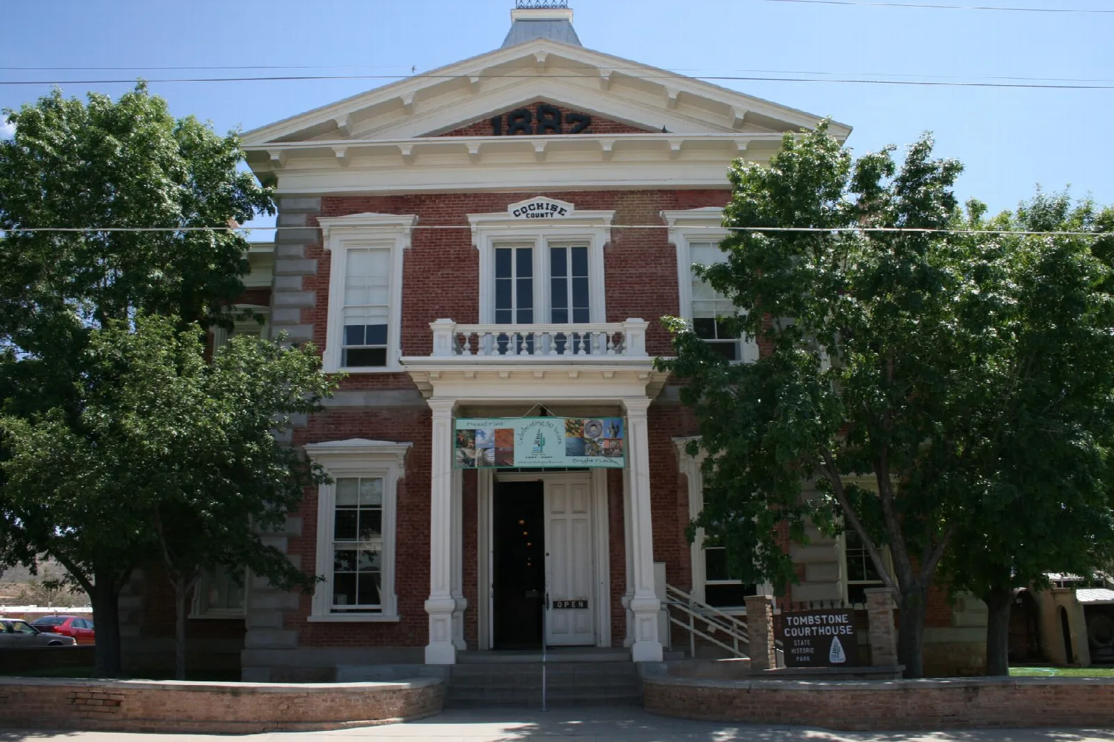 Red-brick two-story courthouse with white trim and a front porch, framed by trees