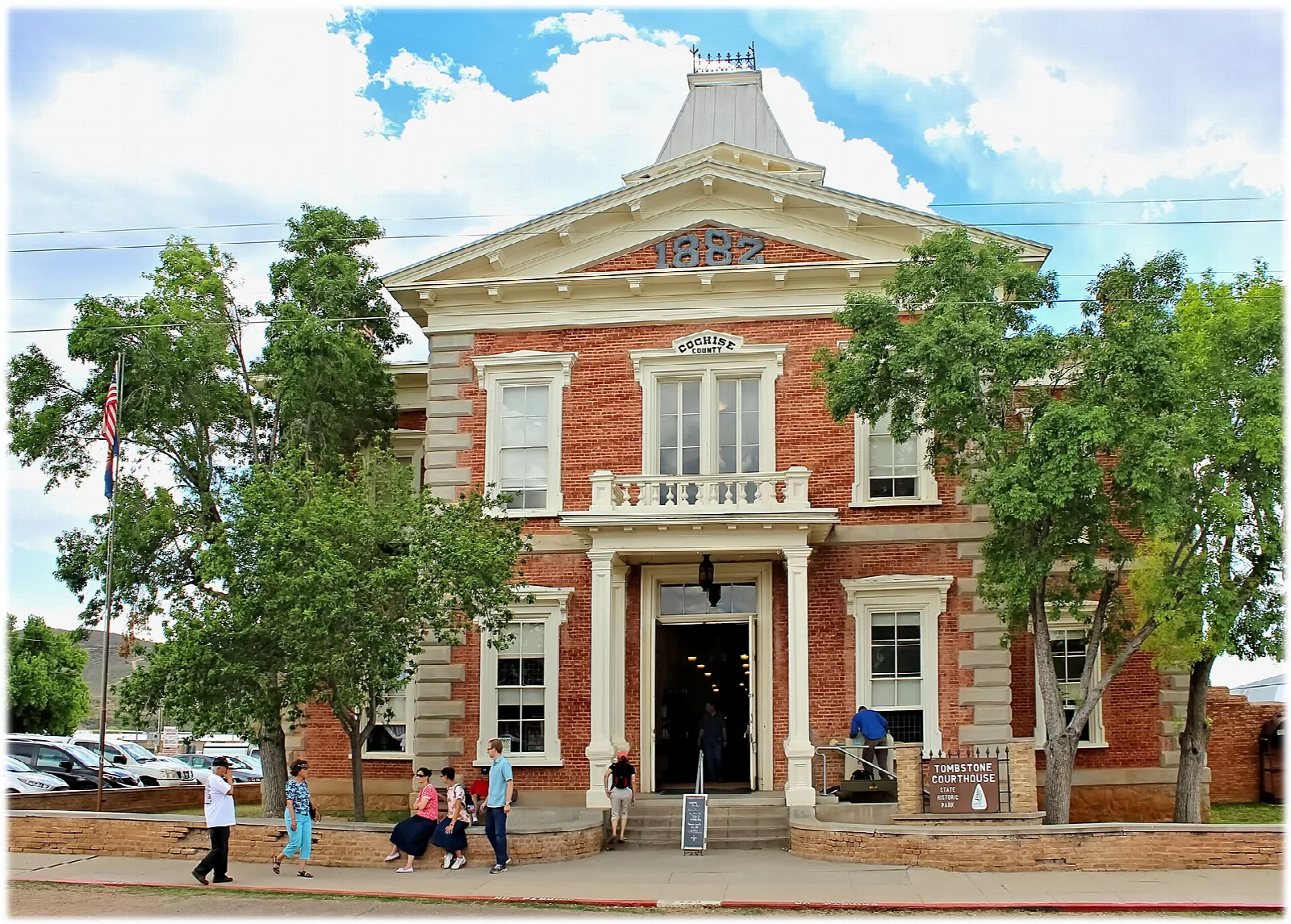 Brick courthouse front with visitors walking on the sidewalk under puffy clouds