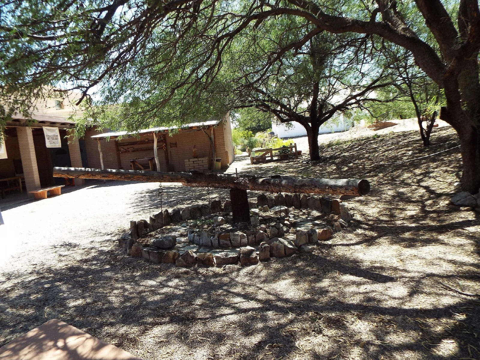 Old wooden beam and stone ring in a shaded yard under mesquite trees