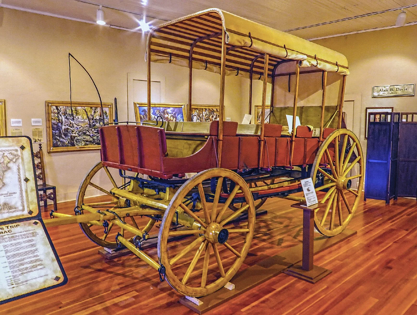 Painted covered wagon on display in a museum room with wood floors