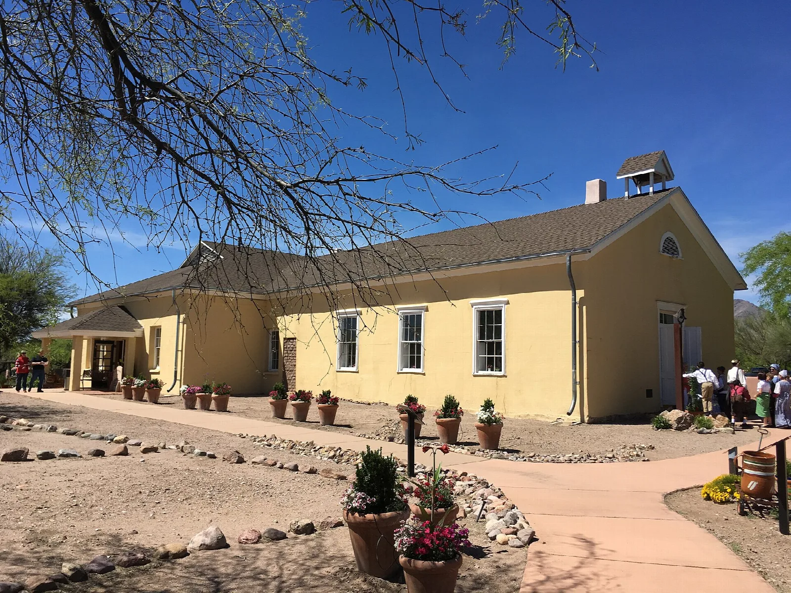 Yellow one-room schoolhouse with a bell cupola beside a gravel path