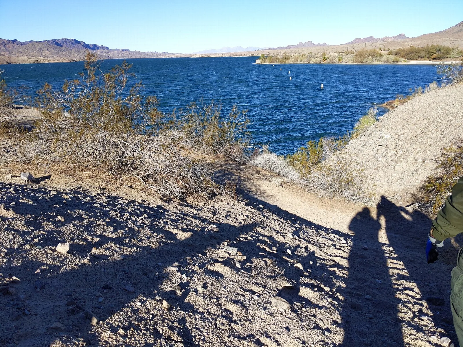 Dirt trail leading down to a blue lake with mountains beyond