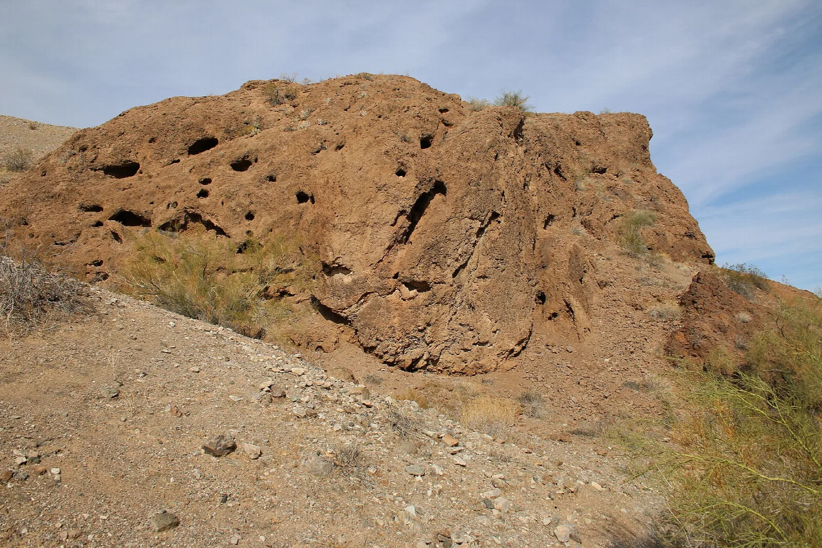Weathered reddish rock outcrop with small holes under blue sky