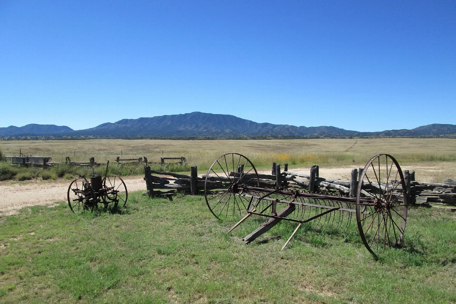 Old horse-drawn farm equipment in a grassy valley with a mountain beyond