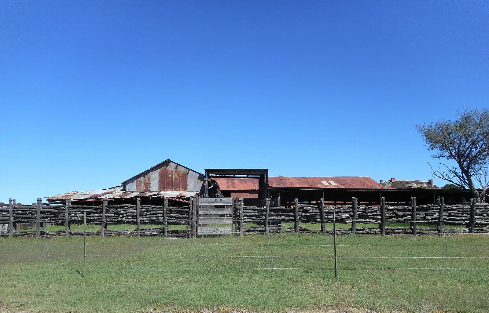 Weathered barn and a wooden pole corral under a blue sky