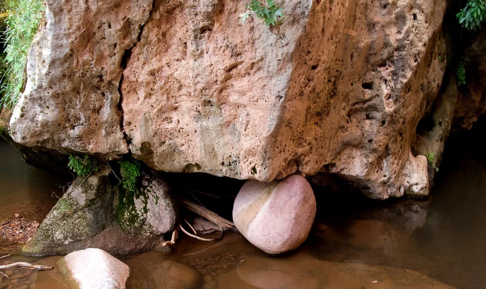Large rust-colored rock with a round boulder wedged beneath it over a creek