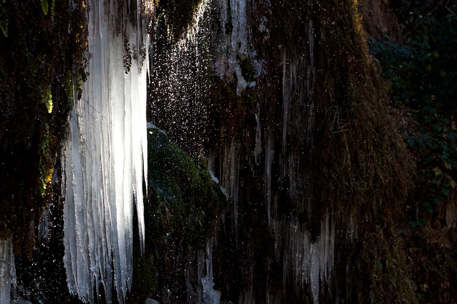 Tall column of ice hanging beside a dark mossy rock wall