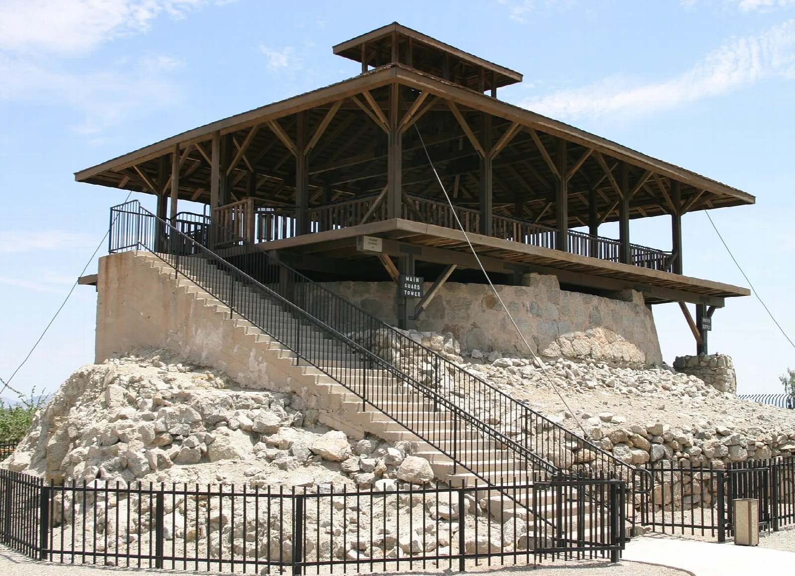 Wooden guard tower with a stair on a rocky base behind an iron fence