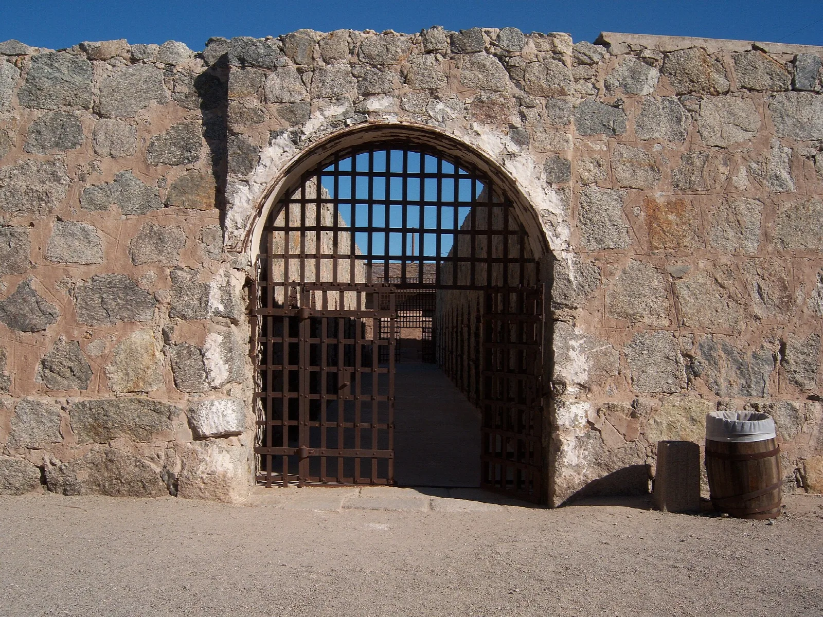 Stone wall with an arched iron-barred gate and a barrel beside it