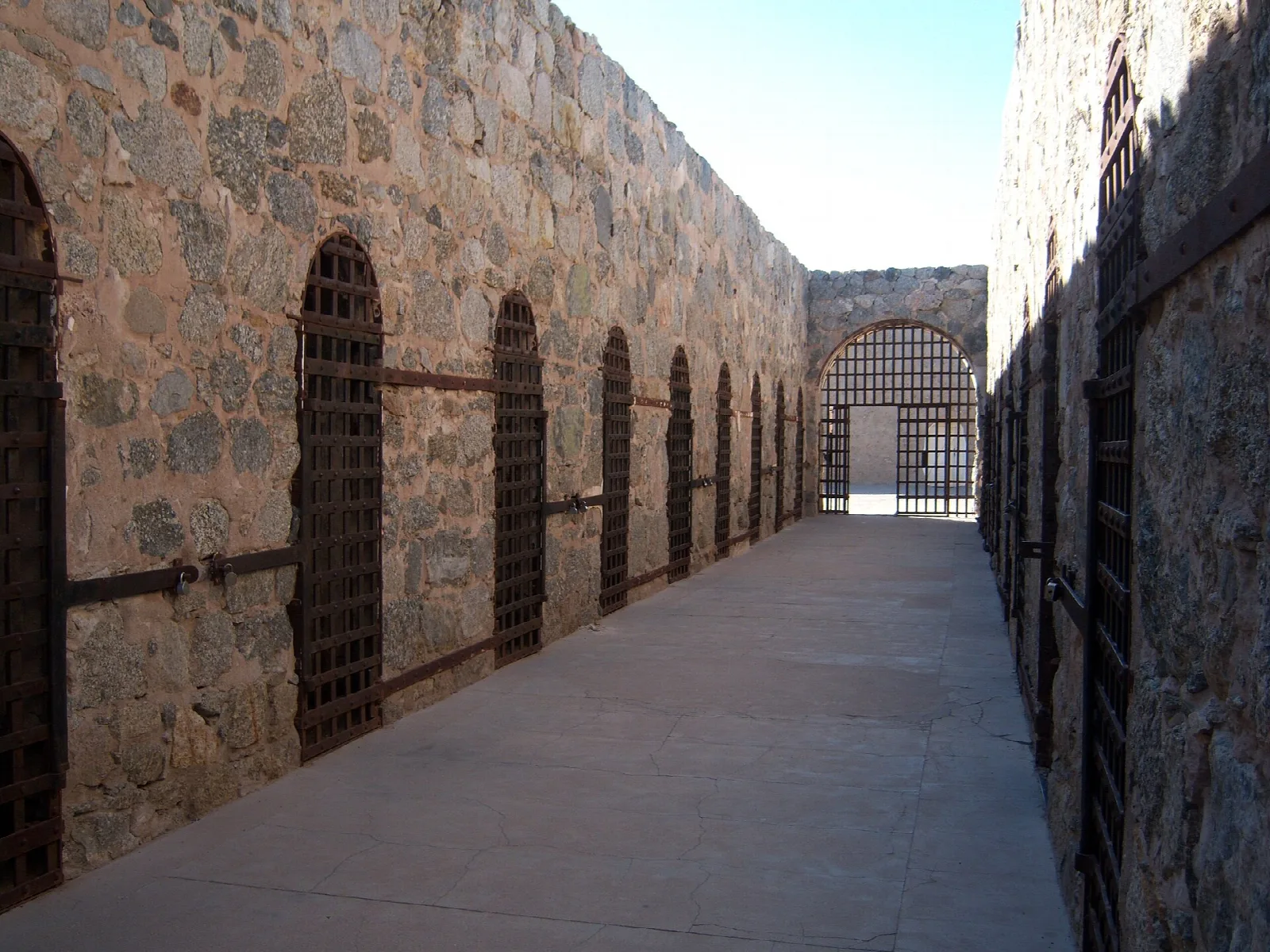 Narrow stone cell block corridor with barred cell doors on both sides