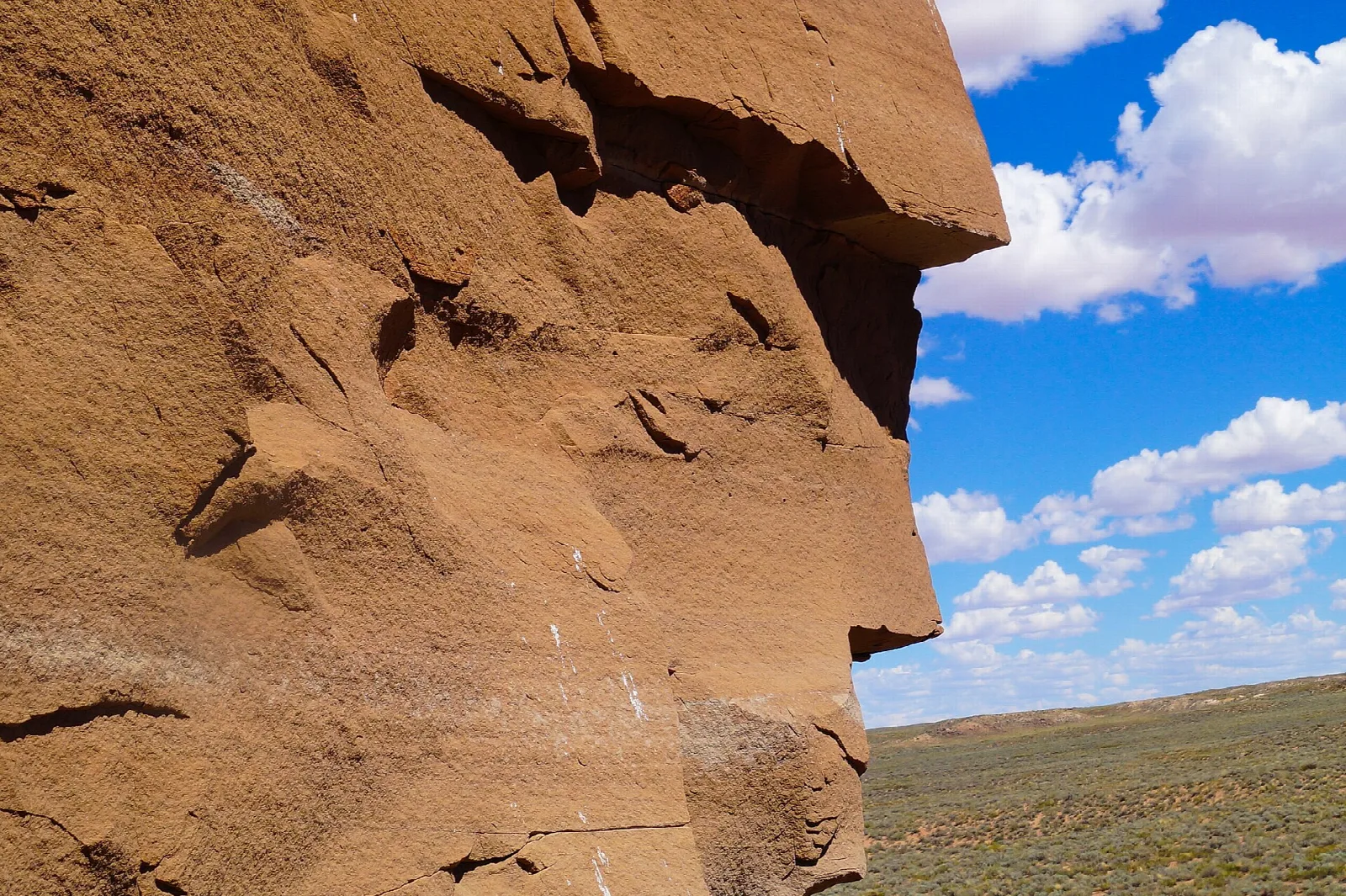Large sandstone rock face against blue sky and open plain